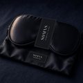 SOMNS black mulberry silk eye mask with a black SOMNS band, resting on its black silk pouch