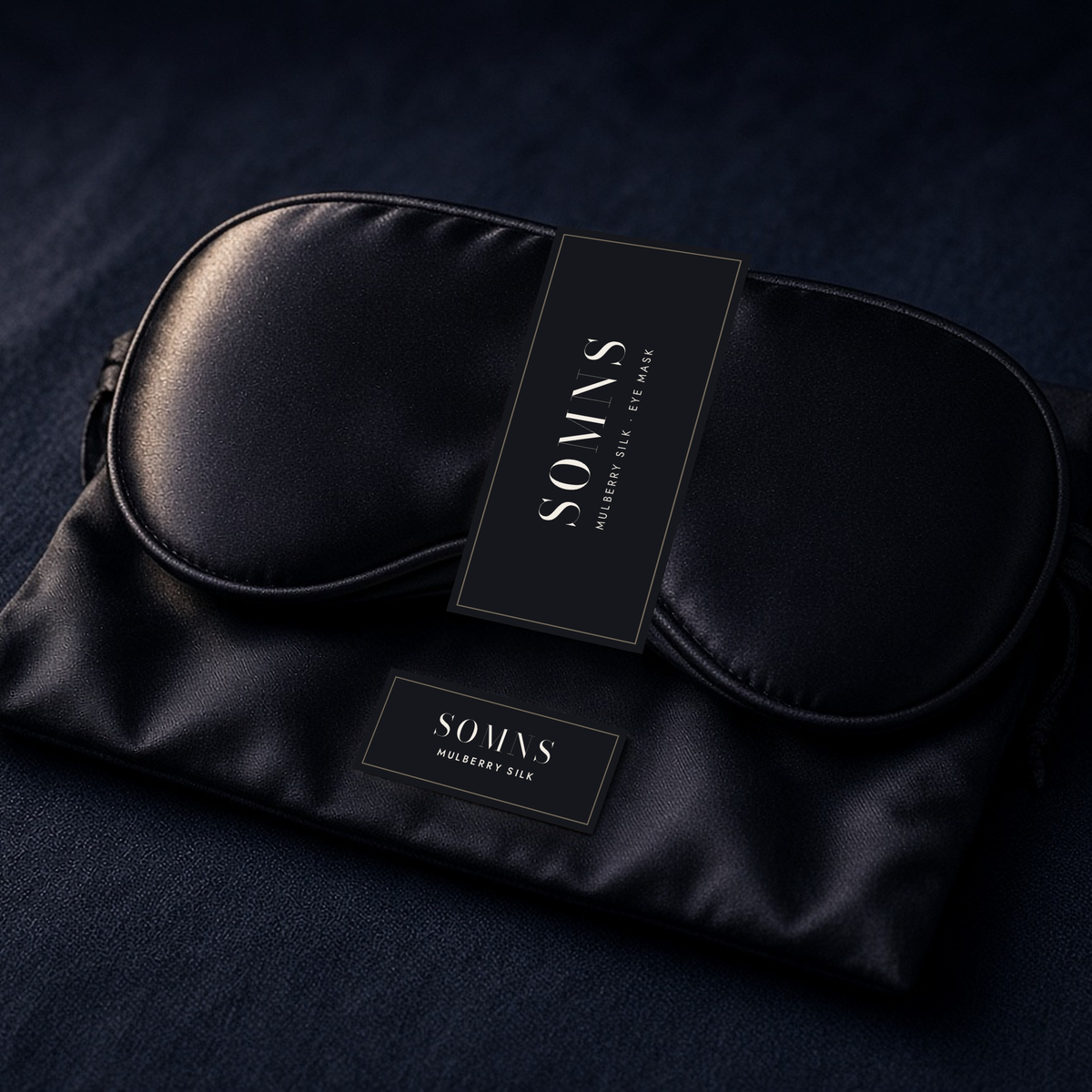 SOMNS black mulberry silk eye mask with a black SOMNS band, resting on its black silk pouch