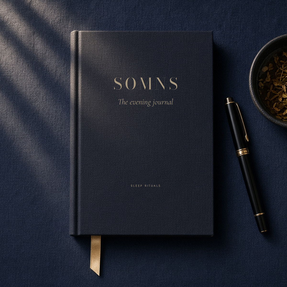 SOMNS Evening Journal: a navy linen-bound notebook with SOMNS and The evening journal in champagne foil, with a ribbon marker