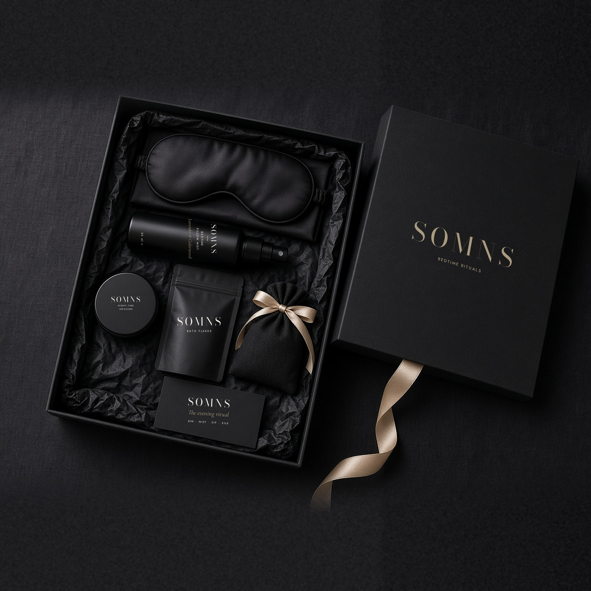 Opened SOMNS Midnight Silk box on black tissue with the pillow mist, silk eye mask, tea tin, bath flakes and ritual card inside