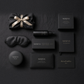 SOMNS Signature gift set flat-lay on black: Bedtime Pillow Mist 50 ml and carton at the centre, with a black silk pillowcase, silk eye mask, glass candle in a black SOMNS box, bath flakes, tea tin, evening journal and gift card