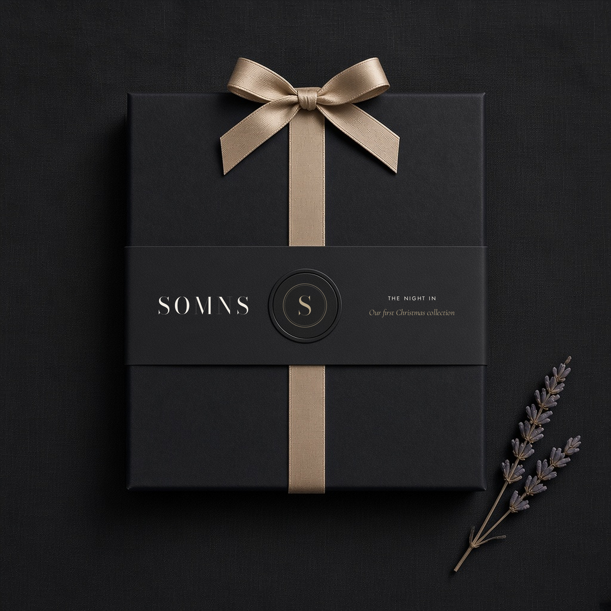 Black SOMNS gift box with a black The Night In sleeve, champagne monogram seal and champagne satin ribbon